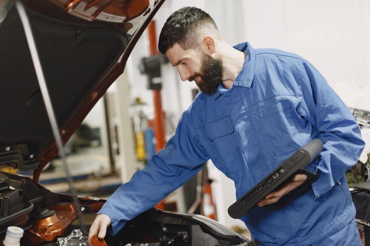 Monteur in blauwe overall controleert de motor met een diagnosetablet
